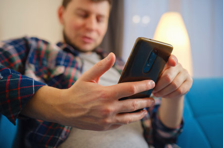 Happy man using mobile phone on a couch at home. Closeup of young man using smartphone to checking...