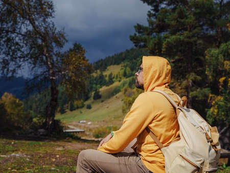 Man resting after hike with beautiful view of snowy mountain peaks. Wandering lifestyle, adventure concept autumn vacation outdoors, alone in the wild. Travel to North Caucasus, Arkhyz, Russiaの写真素材