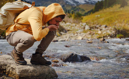 Man drinks clear water from mountain river. Wandering lifestyle, adventure concept autumn vacation outdoors, alone in the wild. Travel to North Caucasus, Arkhyz, Russiaの写真素材