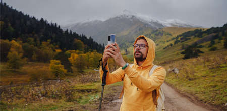 Man makes beautiful photos on smartphone for social network. Wandering lifestyle, adventure concept autumn vacation outdoors, alone in the wild. Travel to North Caucasus, Arkhyz, Russiaの写真素材