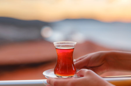 Woman drinking turkish tea from traditional turkish teacup and enjoys panorama over sunset of Kas resort town of Mediterranean sea in Turkeyの写真素材