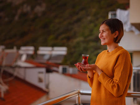Woman drinking turkish tea from traditional turkish teacup and enjoys panorama over sunset of Kas resort town of Mediterranean sea in Turkeyの写真素材