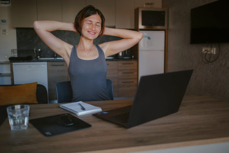 Asian creative female freelancer holding hands behind and close eye in front of laptop on desk....