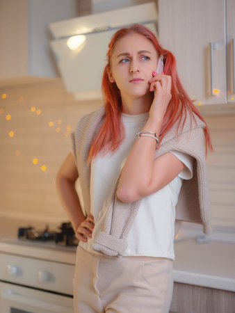 Young beautiful caucasian woman using cell phone in kitchen. home office. beautiful lady having...