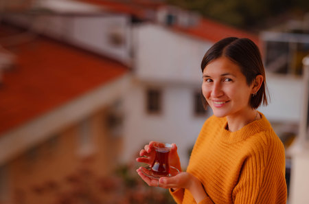 Woman drinking turkish tea from traditional turkish teacup and enjoys panorama over sunset of Kas resort town of Mediterranean sea in Turkeyの写真素材