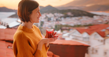 Woman drinking turkish tea from traditional turkish teacup and enjoys panorama over sunset of Kas resort town of Mediterranean sea in Turkeyの写真素材
