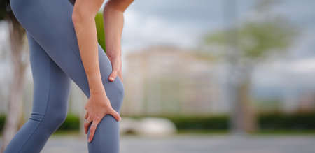 pain and discomfort from knee injury during morning run. Young woman was running in park and suddenly felt sharp pain in knee joint due to dislocation or rupture of meniscus.の写真素材