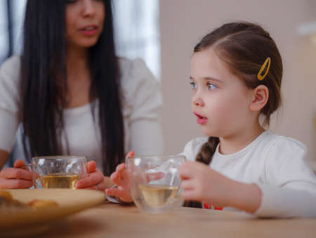Family drinking tea with cookies on kitchen at home. Mother and daughter having fun, happy moment together at home.の写真素材