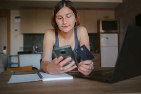 young asian woman at home, remote work at laptop. shopping online at home, lady is holding credit card and using smartphone and computer.の写真素材