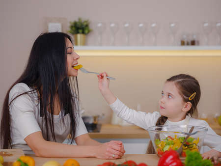 Happy mother and daughter enjoy prepare freshly salad together in kitchen. Healthy food at home. Healthy Lifestyle and Eating Concept. little influencer filming blog about healthy eatingの写真素材