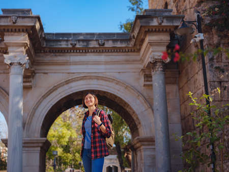 travel to Turkey. Happy asian female tourist traveler with backpack walks in old city. Woman against backdrop of Hadrian's gate - popular attraction in old city of Antalyaの写真素材