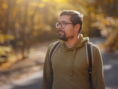 Young handsome man posing in autumn forest. young hipster guy with backpack , traveler standing in...