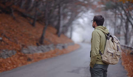 Young handsome man posing in autumn forest on road. young hipster guy with backpack , traveler standing in woods, Hiking, Forest, Journey, active healthy lifestyle, adventure, vacation concept.の写真素材