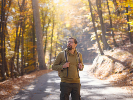 Young handsome man posing in autumn forest. young hipster guy with backpack , traveler standing in...