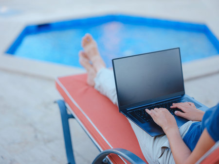 Young business woman working at computer by hotel pool. Young lady downshifter working at laptop and...