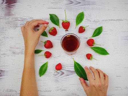 Fresh organic strawberries and black tea in glass cup with woman hand , over white background. Vegetarian healthy food concept.の写真素材
