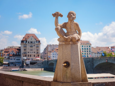 BASEL, SWITZERLAND, JULY 7, 2022: Fountain Knabe mit Fisch what does mean boy with the fish close to Rhine river and Mittlere Brucke middle bridge in Basel city.のeditorial素材