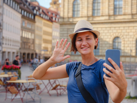 summer female solo trip to Europe, happy young woman walking on european street, on the town building background in Munich. making pictures or selfies on the sunny day.の写真素材