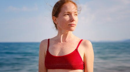 Beautiful ginger woman in red bikini on tropical beach. Portrait of happy young lady smiling at sea. Happy girl with red hair and freckles enjoying the sun. concept of safe interaction with sunの写真素材