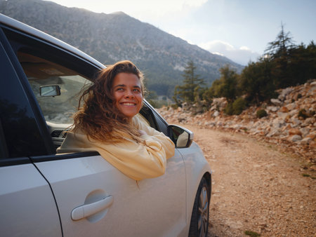 Woman on road trip traveling by rental car . adventure lifestyle vacations vibes outdoor sunset Turkey mountains forest, Fethie , Babadag mount. Happy female raising her hand out of the car window.の写真素材