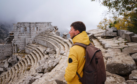 Autumn walk , man in yellow jacket looks at the ancient amphitheatre in city Termessos Ancient City, Turkey. Turkeys most outstanding archaeological sites and one of main tourist center.の写真素材