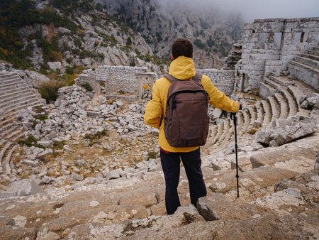 Autumn walk , man in yellow jacket looks at the ancient amphitheatre in city Termessos Ancient City, Turkey. Turkeys most outstanding archaeological sites and one of main tourist center.の写真素材