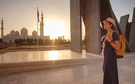 travel to the United Arab Emirates, Happy young asian female traveler with backpack and hat in Wahat Al Karama or Oasis of Dignity, permanent memorial for its martyrs, and Shaikh Zayed Grand Mosque.の写真素材