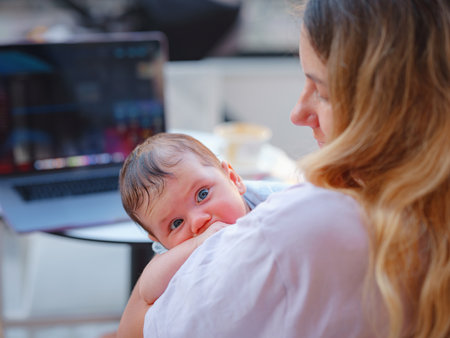 Diverse people portrait. Creative businesswoman balancing work and motherhood. Beautiful young mother working with laptop computer and breastfeeding, holding and nursing her newborn baby at cafe.の写真素材