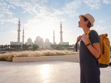 travel to the United Arab Emirates, Happy young asian female traveler with backpack and hat in Wahat Al Karama or Oasis of Dignity, permanent memorial for its martyrs, and Shaikh Zayed Grand Mosque.の写真素材