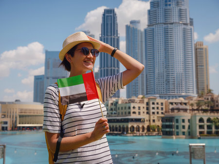 Enjoying travel in United Arabian Emirates. Young woman with yellow backpack with the flag of the United Arab Emirates walking on Dubai Downtown in sunny summer day.の写真素材