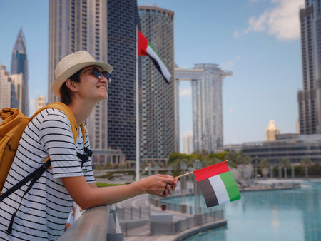 Enjoying travel in United Arabian Emirates. Young woman with yellow backpack with the flag of the United Arab Emirates walking on Dubai Downtown in sunny summer day.の写真素材