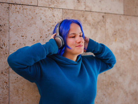 young caucasian blue hair woman listening music with headphones on the street - serene, enjoying, music concept. Music lover enjoying songsの写真素材
