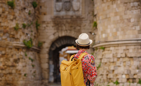 summer trip to Rhodes island, Greece. Young Asian woman in ethnic red dress walks through streets of city of Rhodes.の写真素材