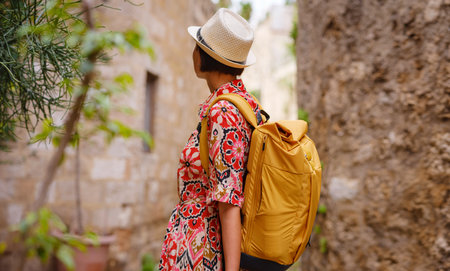 Young Asian woman in ethnic red dress walks and looks at cozy narrow streets of old city. Tourism, vacation, and discovery concept, female traveler visiting southern Europe, Rhodes island, Greece.の写真素材