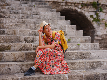 Young Asian woman in red dress walks through streets of Rhodes. woman resting on old house steps in fortress Rhodes. Tourism, vacation, and discovery concept, female traveler visiting southern Europe.の写真素材