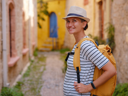 summer trip to Rhodes island Greece. Young Asian woman in striped tshirt and hat walks Street of Knights of Fortifications castle. female traveler visiting southern Europe.の写真素材