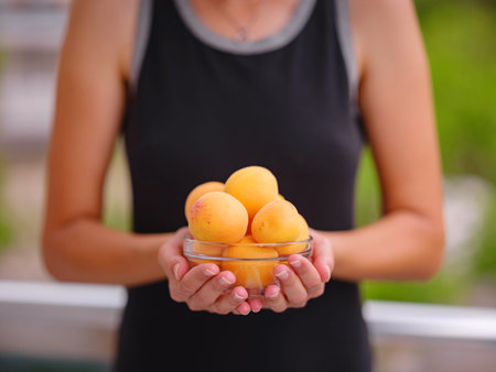 woman holding bowl of fresh apricots in her hands while standing in garden. Harvest background. Organic fruits. Farmers market.の写真素材
