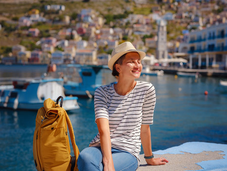 Nice asian Happy Female with backpack Enjoying her holidays on Symi Islands. View of port Symi or Simi, is tiny island of Dodecanese, Greece, calm atmosphere and fabulous architecture.の写真素材