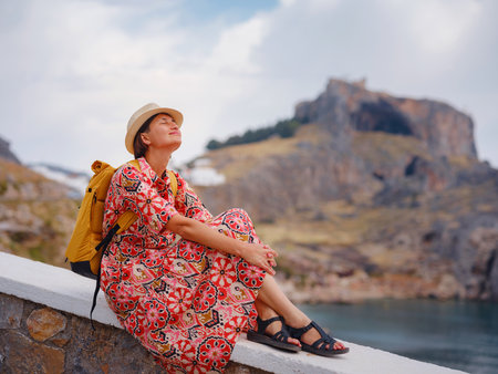Nice Happy Female Enjoying Greek Islands. Travel to Greece, Mediterranean islands outside tourist season. Having fun at stunning views on sea resort and old town of Lindos on mountainの写真素材