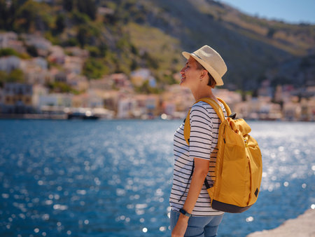 Nice asian Happy Female with backpack Enjoying her holidays on Symi Islands. View of port Symi or Simi, is tiny island of Dodecanese, Greece, calm atmosphere and fabulous architecture.の写真素材