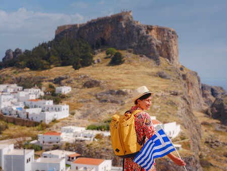 Young traveling woman with national greek flag enjoying view of Lindos. Travel to Greece, Mediterranean islands outside tourist season.の写真素材