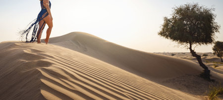 Desert adventure. Young Arabian Woman in sexy boho blue makrame dress in sands dunes of UAE desert at sunset. The Dubai Desert Conservation Reserve, United Arab Emirates.の写真素材