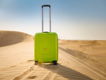 bright light green or yellow suitcase in sands of desert dunes. Concept and idea of travel to United Arab Emirates, Dubai sands at sunset. Summer holiday travel conceptの写真素材