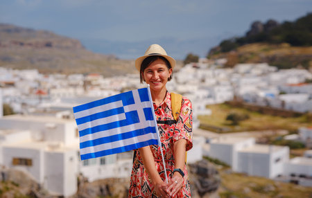 Young traveling woman with national greek flag enjoying view of Lindos. Travel to Greece, Mediterranean islands outside tourist season.の写真素材