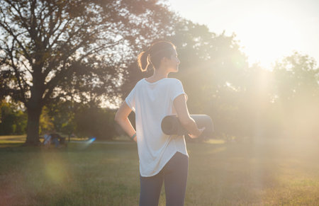 Healthy active lifestyle concept in city park. woman walking with exercise mat through park in summer day, after or before health fitness, wellness exercise or outdoor workout.の写真素材