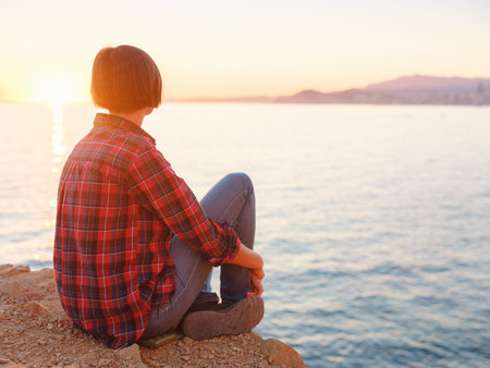 Young woman hiking on rocky beach in Spain, Benidorm. Watching the choppy sea and the bay. traveler enjoying freedom in serene nature landscapeの写真素材