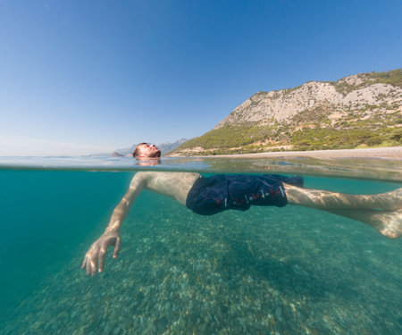 Young male on holidays enjoy floating on a crystal clear water beach of Antalya Turkey. Man swimming with open arms. Relax and tranquilityの写真素材