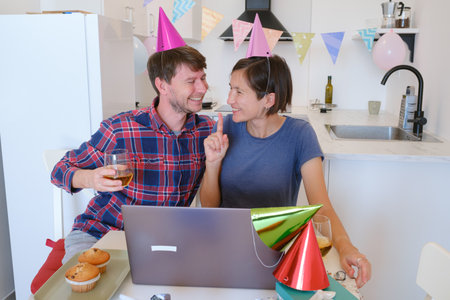 Young family video chatting with relatives on a laptop during a birthday celebration. Smiling and joyful, they connect with loved ones, sharing a special occasion from the comfort of their home.の写真素材