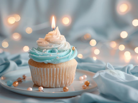 Cupcake with turquoise cream and a burning candle on a white table against a light background, space for text. Birthday celebrationの素材
