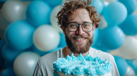 Happy birthday. A photo of an adult man celebrating his birthday, wearing blue balloons and holding cake. The background is a solid color. he smiling joyfully at the camera.の素材